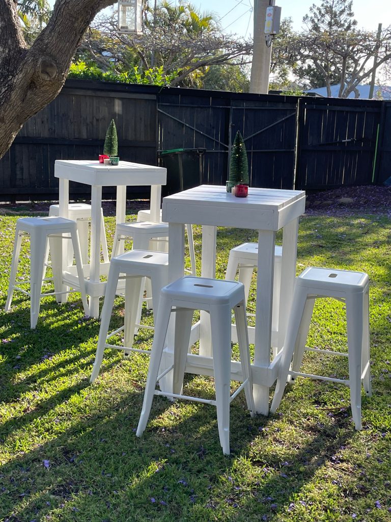 White bar tables and red stools arranged on a lawn for an outdoor party