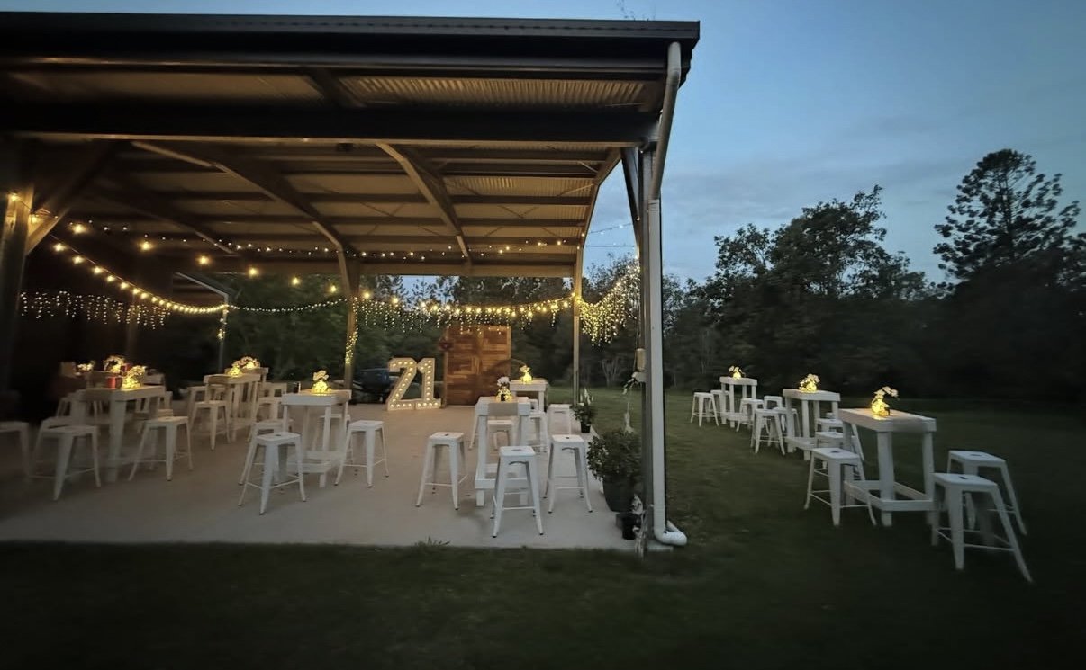 Outdoor dusk party with festoon lights, white bar tables and a 21 marquee light