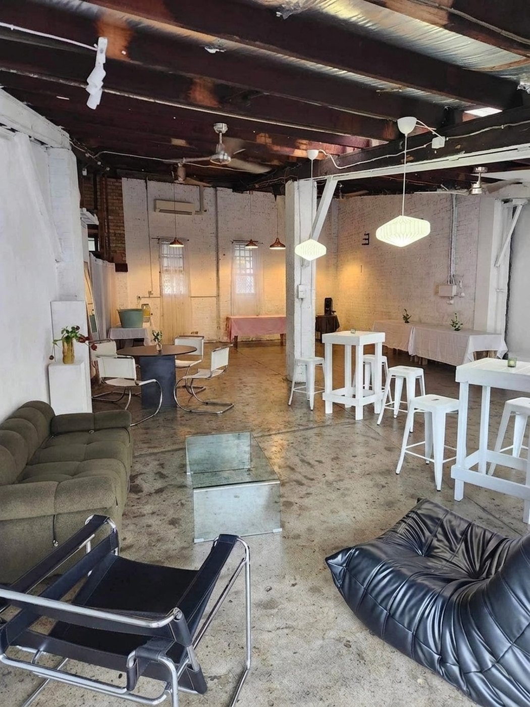 Styled warehouse event space with white bar tables, stools and lounge seating